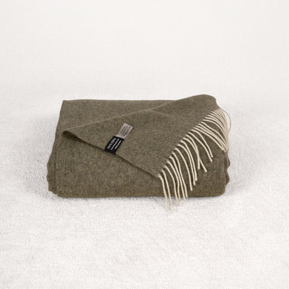 Khaki green cashmere blanket folded on a soft white rug