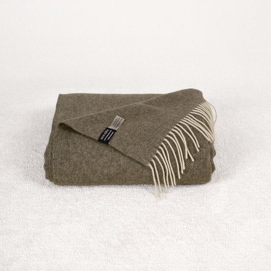 Khaki green cashmere blanket folded on a soft white rug