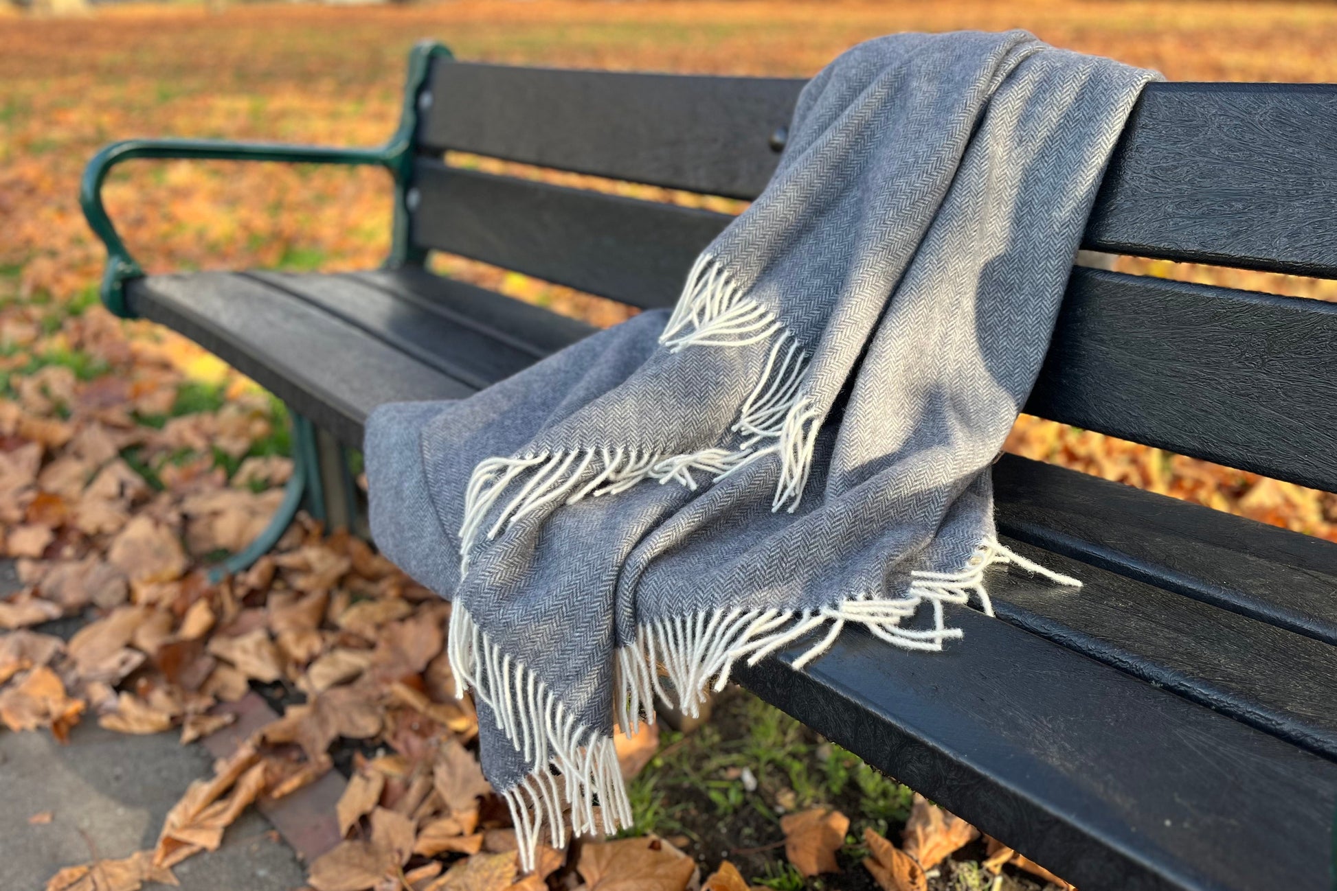 Black-Blue blanket with white fringe draped over a black bench in an outdoor setting with autumn leaves.