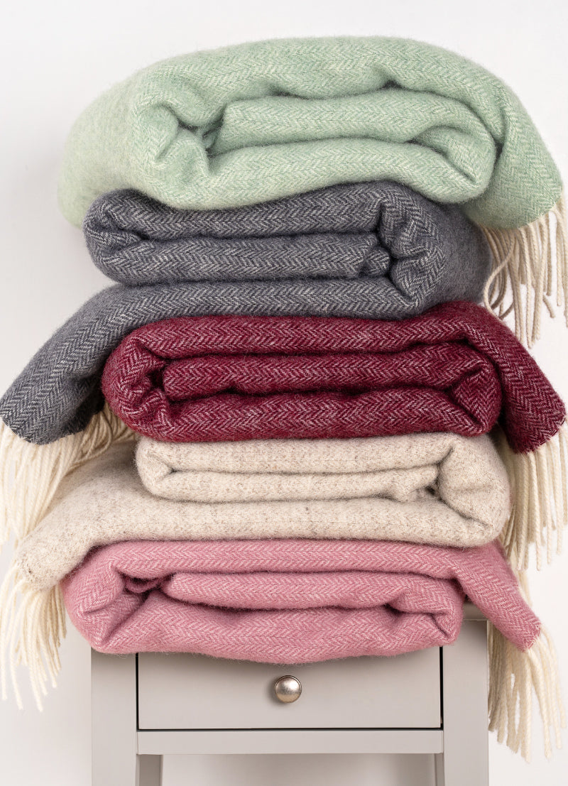 Stack of colorful wool blankets with tassels on a white surface