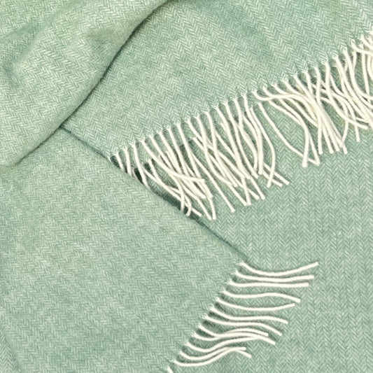 Close-up of a green wool blanket with white fringe details