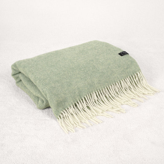 Folded pale green wool blanket with white fringe on a light gray background