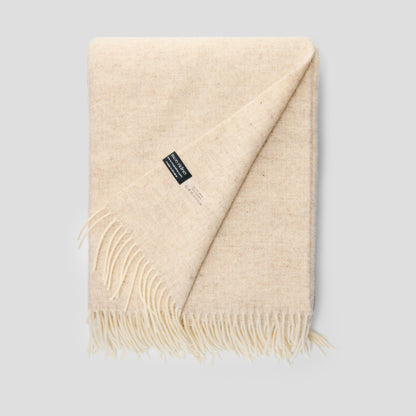 Beige throw blanket with a brand label on a light gray background