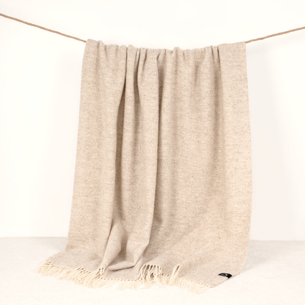 Beige throw blanket with fringes draped over a white surface