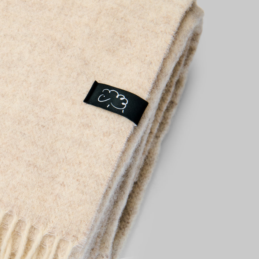Beige blanket folded with a black label featuring a logo on a light gray background