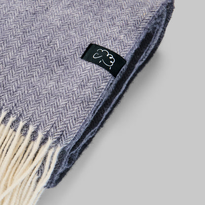 Gray herringbone blanket with a brand logo on a light gray background