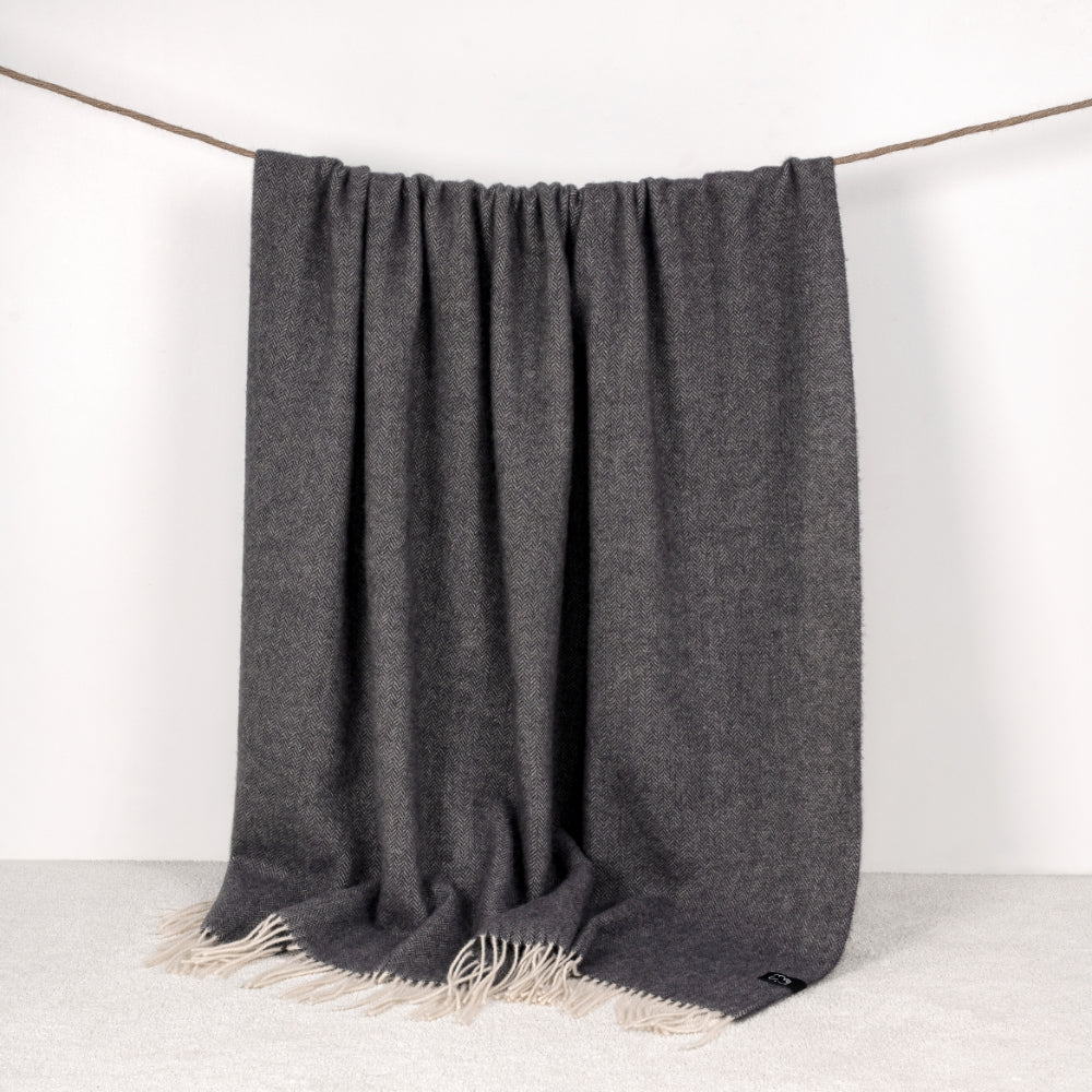 Graphite throw blanket with fringes draped over a white background