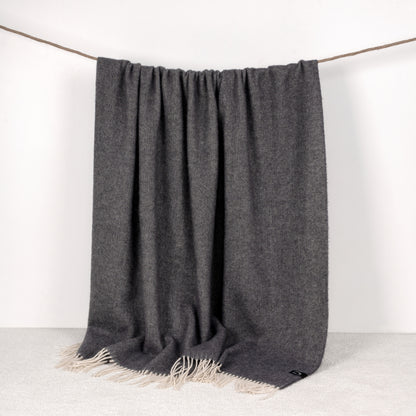 Graphite throw blanket with fringes draped over a white background