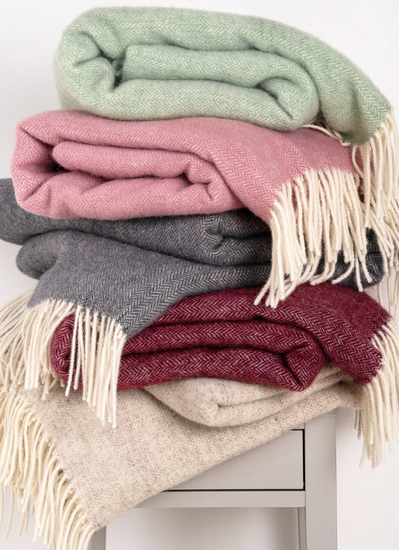 Stack of colorful blankets with fringes on a white surface
