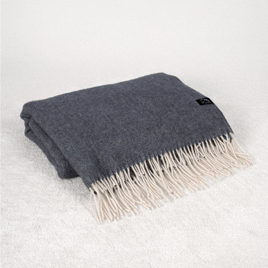 Dark Navy Grey wool blanket with white fringe folded on a soft cream white rug
