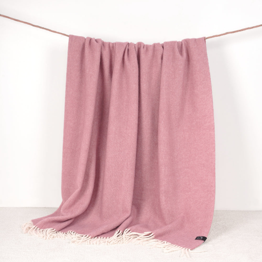 Pink throw blanket with white fringe on a white background