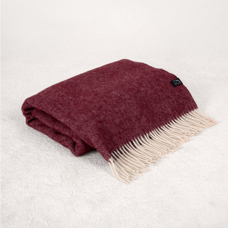 Folded burgundy blanket with white fringe on a light soft background